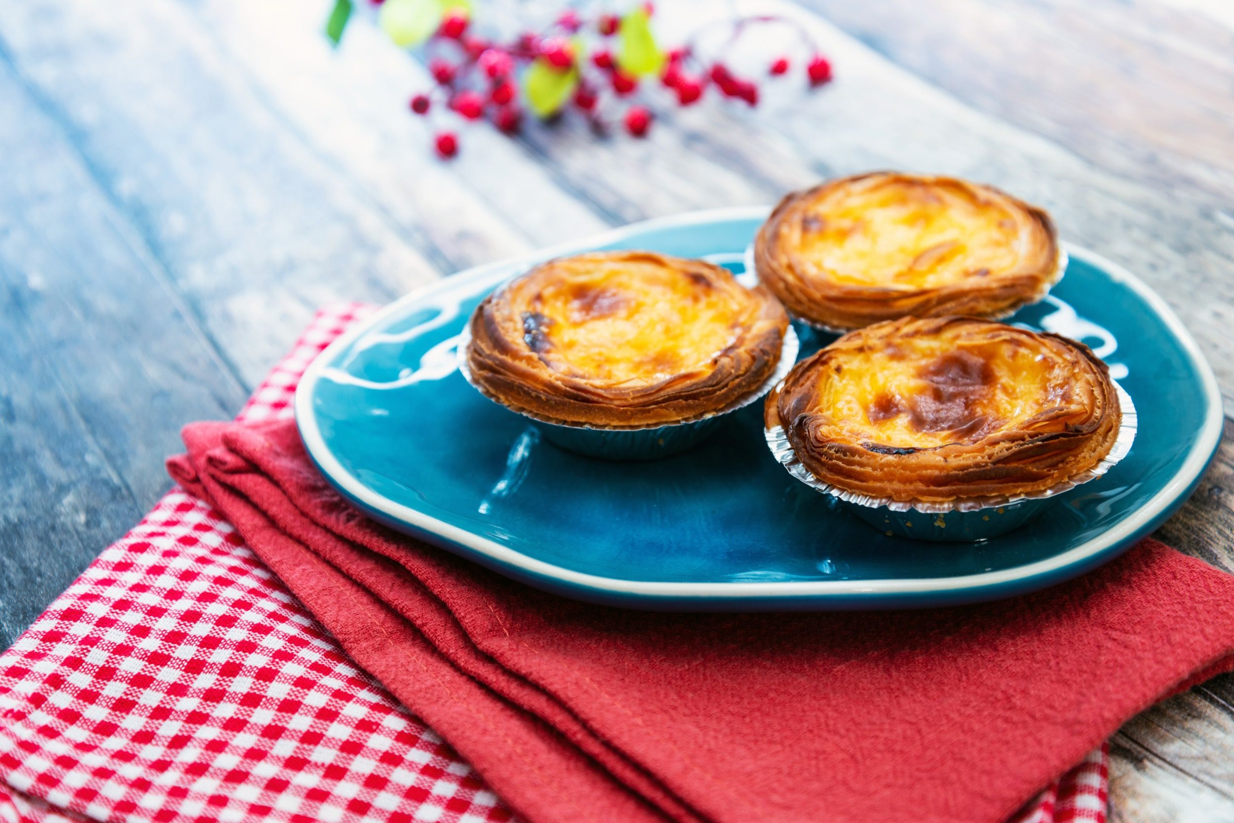 Portugiesische Pastéis de Nata (Blätterteig-Puddingtörtchen) mit Zimtbelag auf blauem Teller, ein klassisches Lissabonner Dessert.