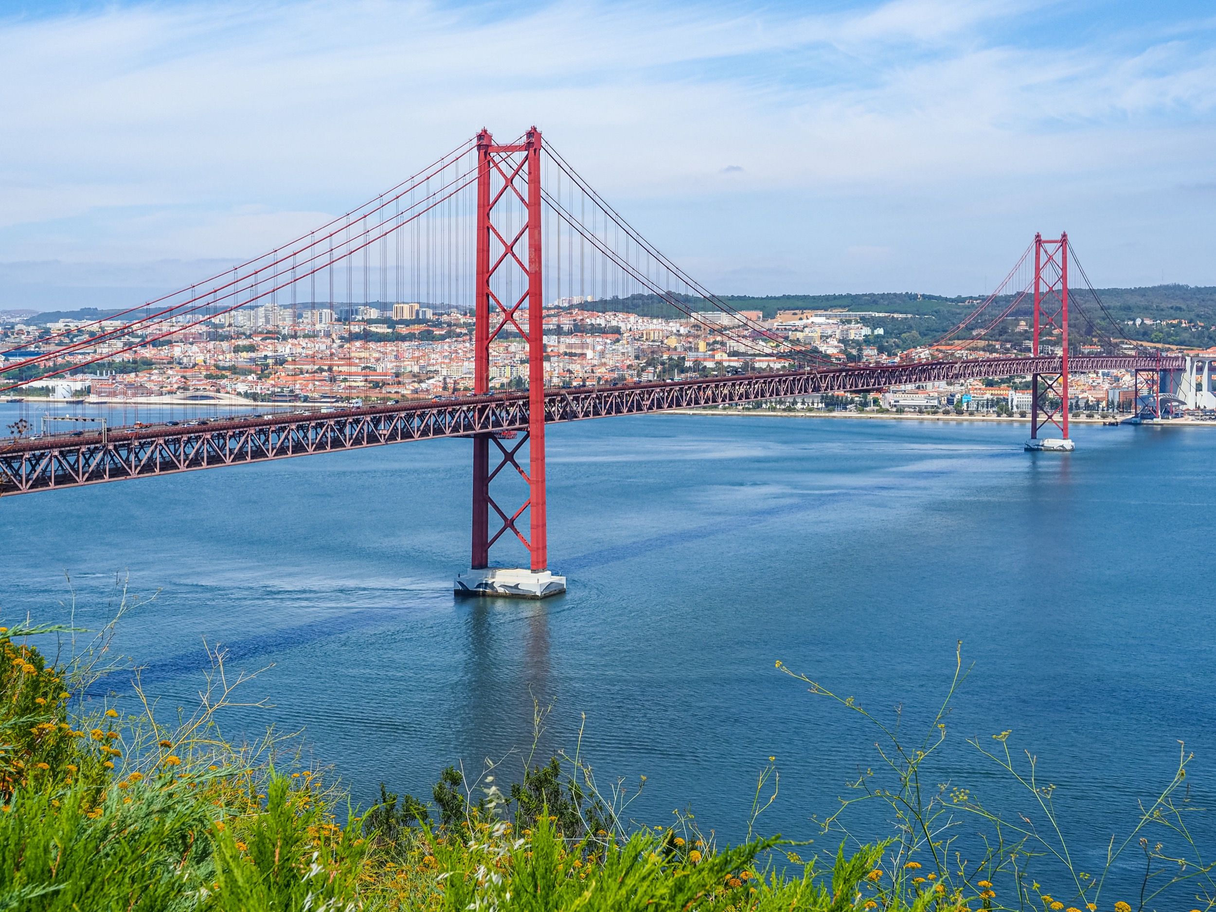 Rote Hängebrücke über den Tejo mit Blick vom Cristo-Rei-Aussichtspunkt auf das Stadtpanorama jenseits des Flusses.